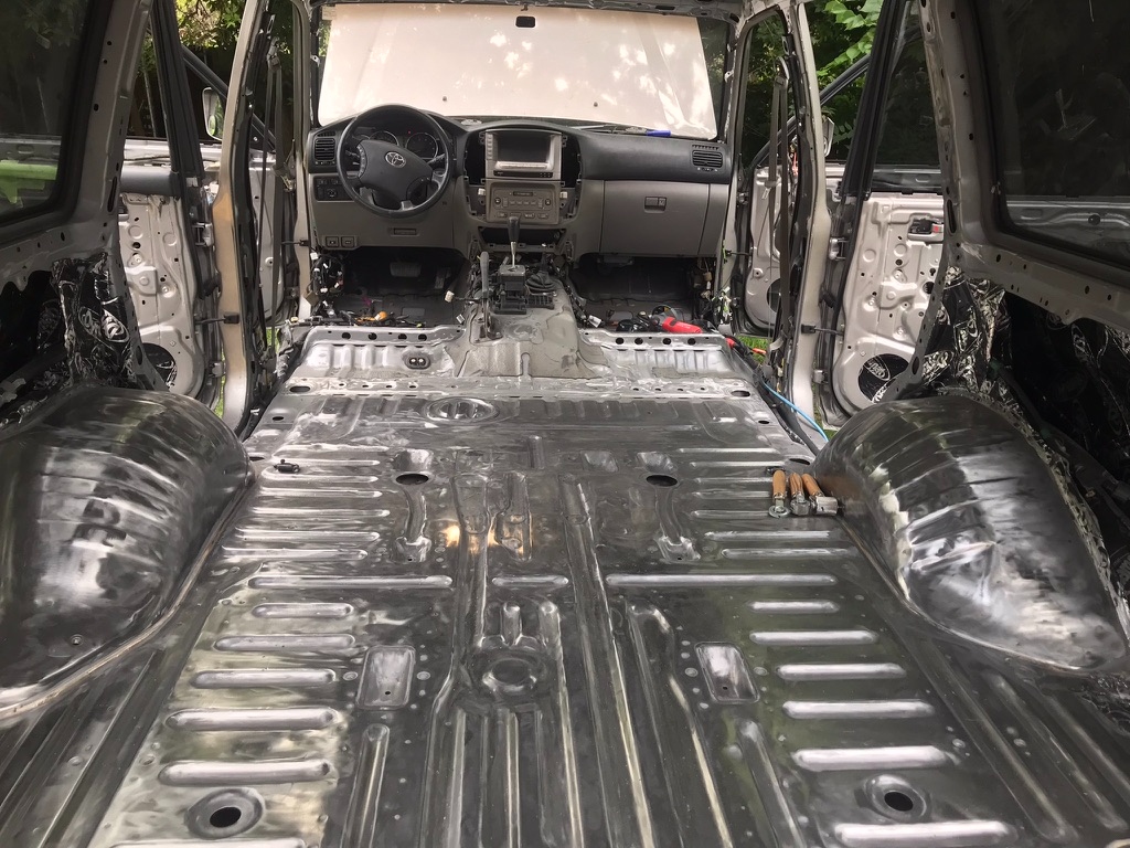 The 2006 Land Cruiser cabin stripped to bare steel — every seat removed, carpet pulled, dash still in place, doors open showing pillar metal. The 40-hour money shot.